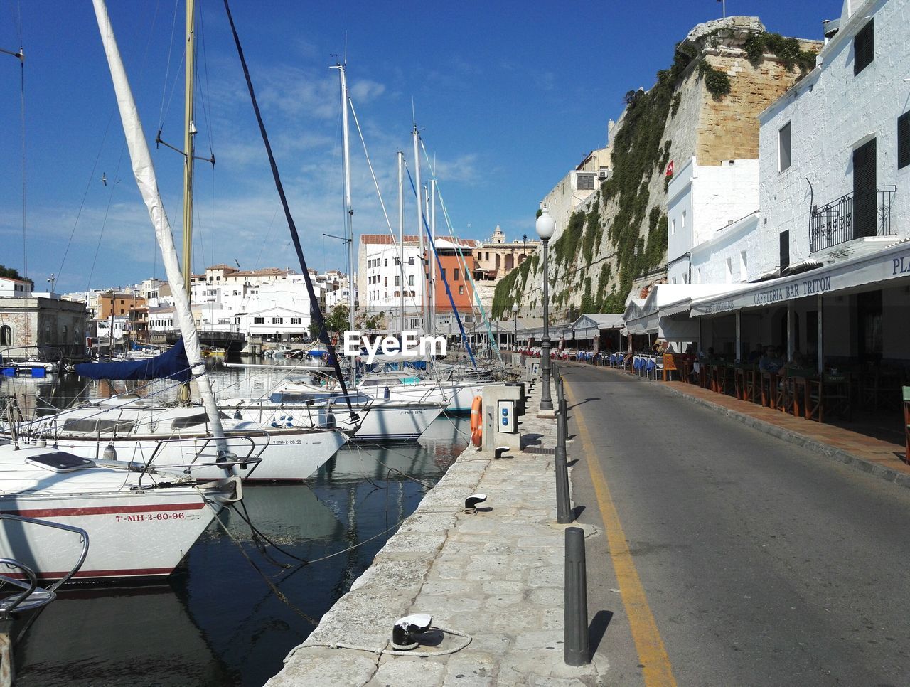 Sailboats moored on sea by street in city