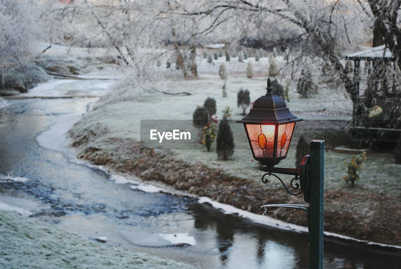 Illuminated street light by canal during winter at dusk