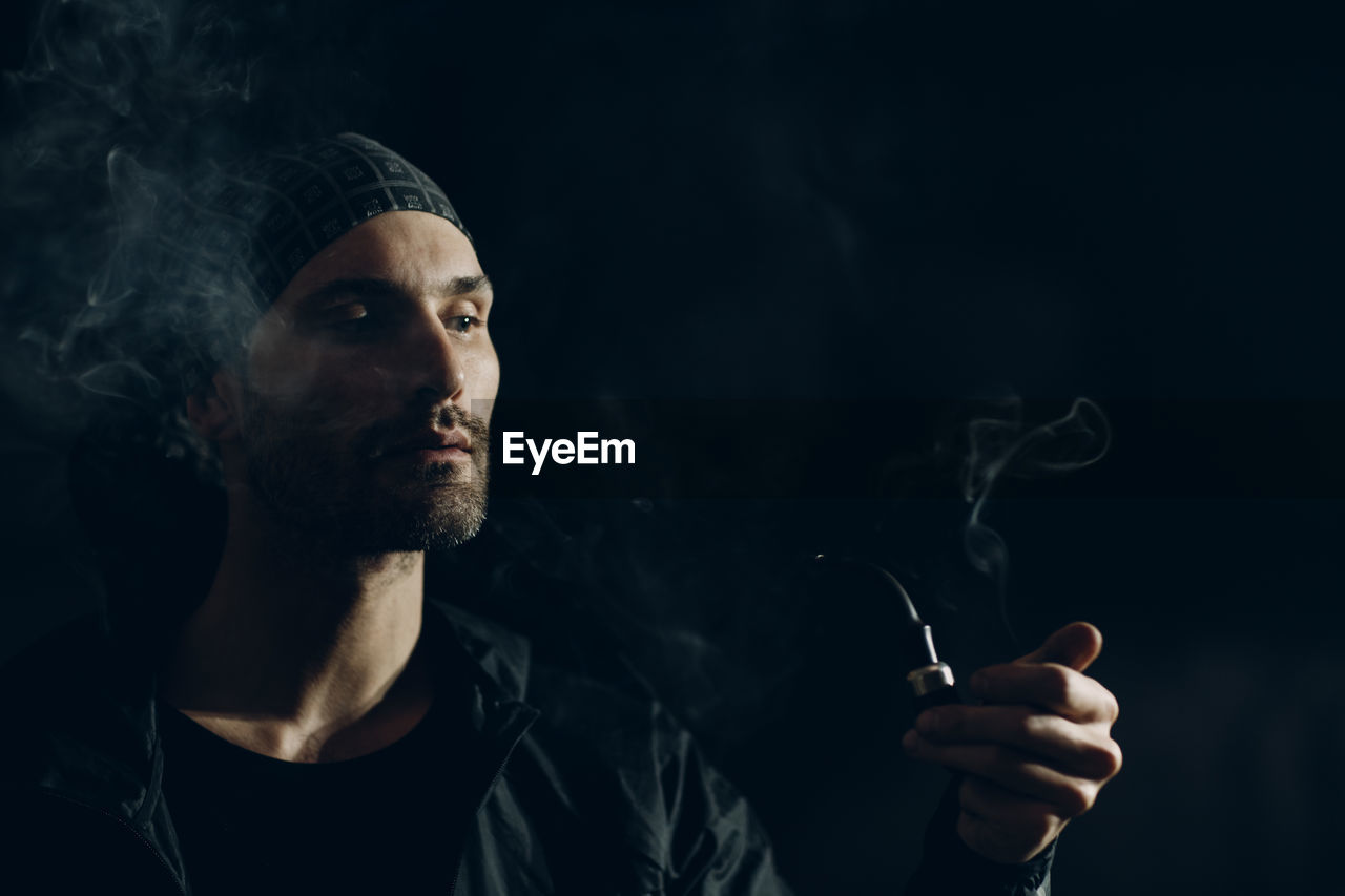 Man smoking pipe against black background