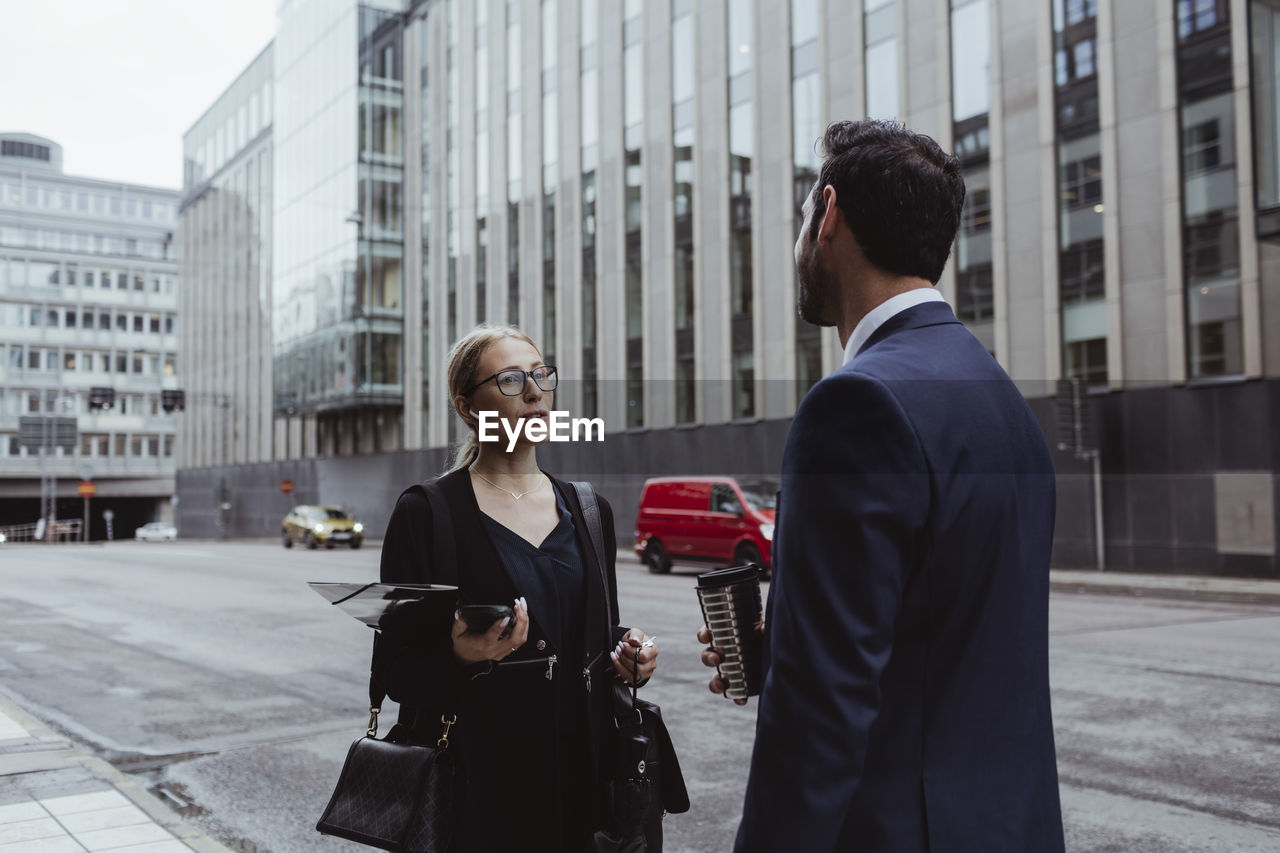 Female entrepreneur with bag talking to coworker in city