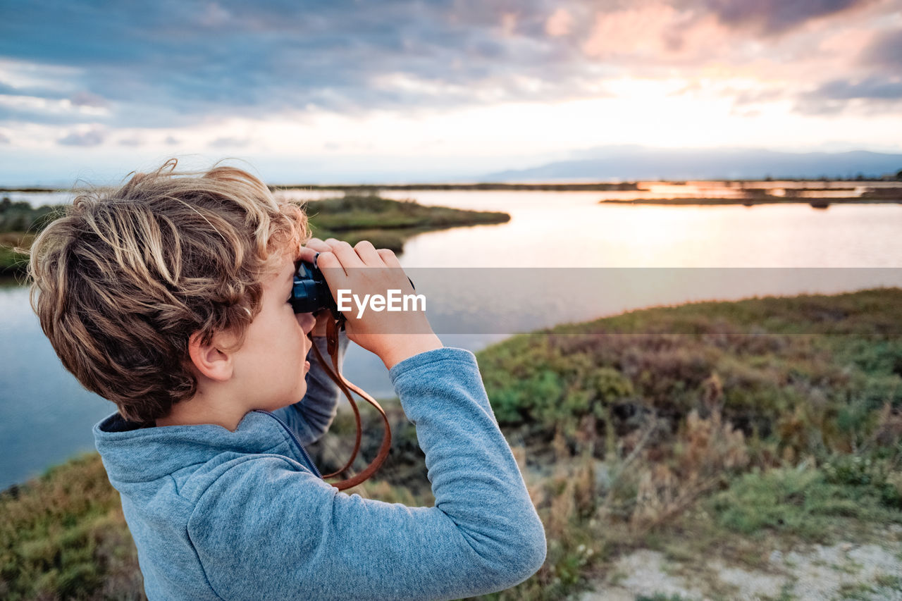 rear view of young woman photographing against sky during sunset