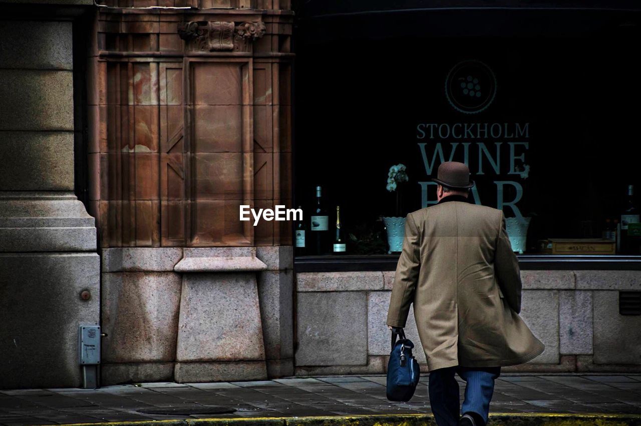 REAR VIEW OF A MAN WALKING IN CITY