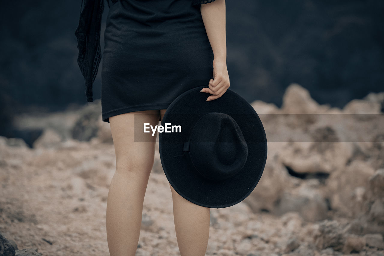 Midsection of woman holding hat while standing on land