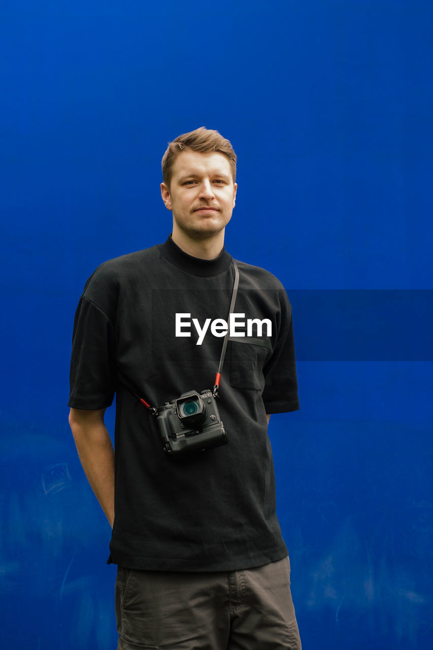 Young man with camera standing against blue background