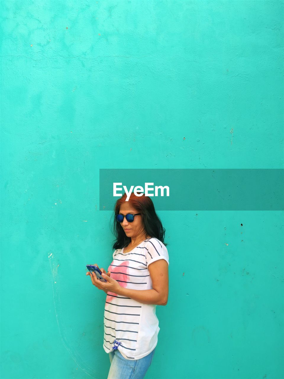 Woman using phone while standing against wall