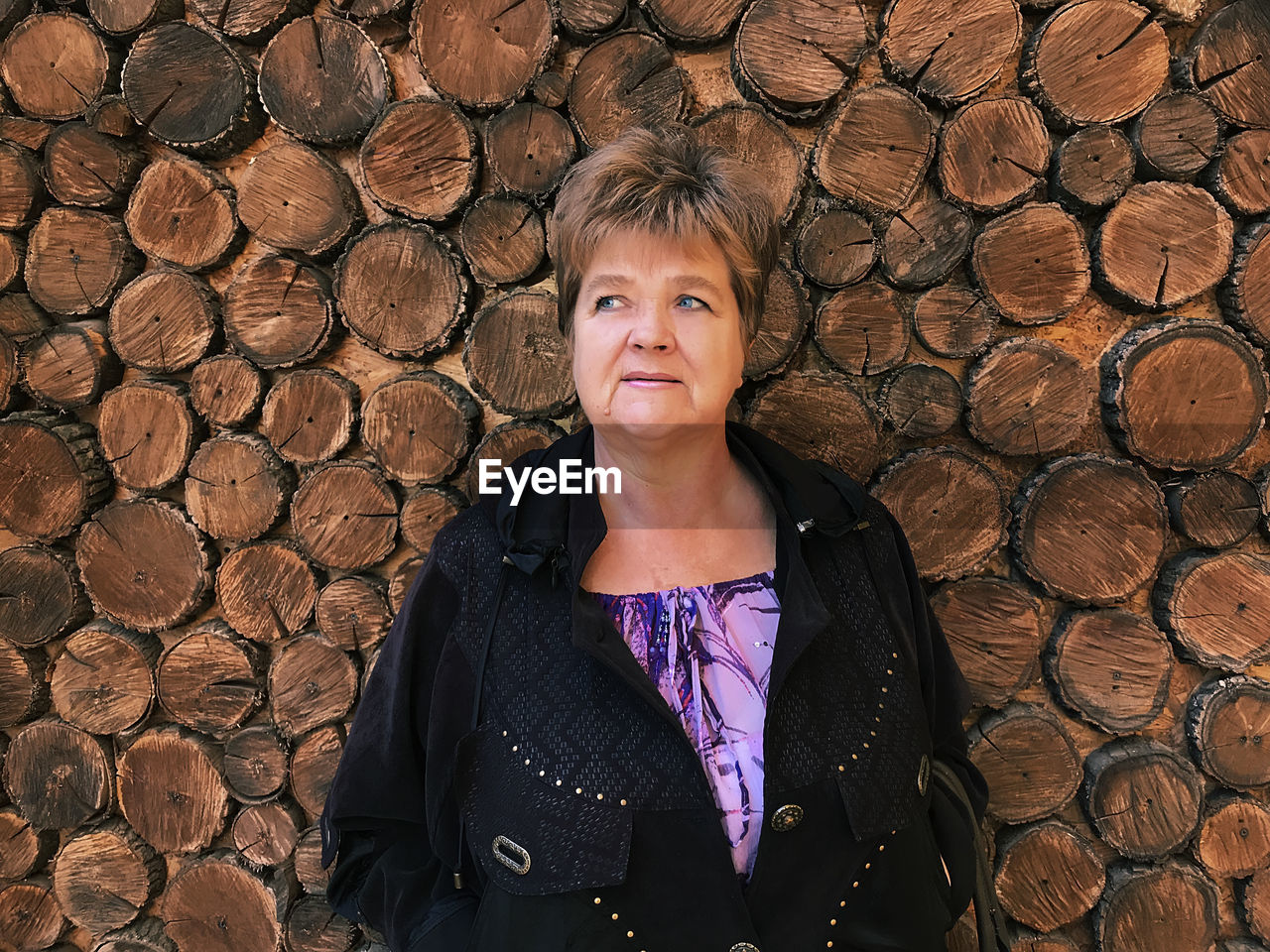 Thoughtful woman standing against stacked logs