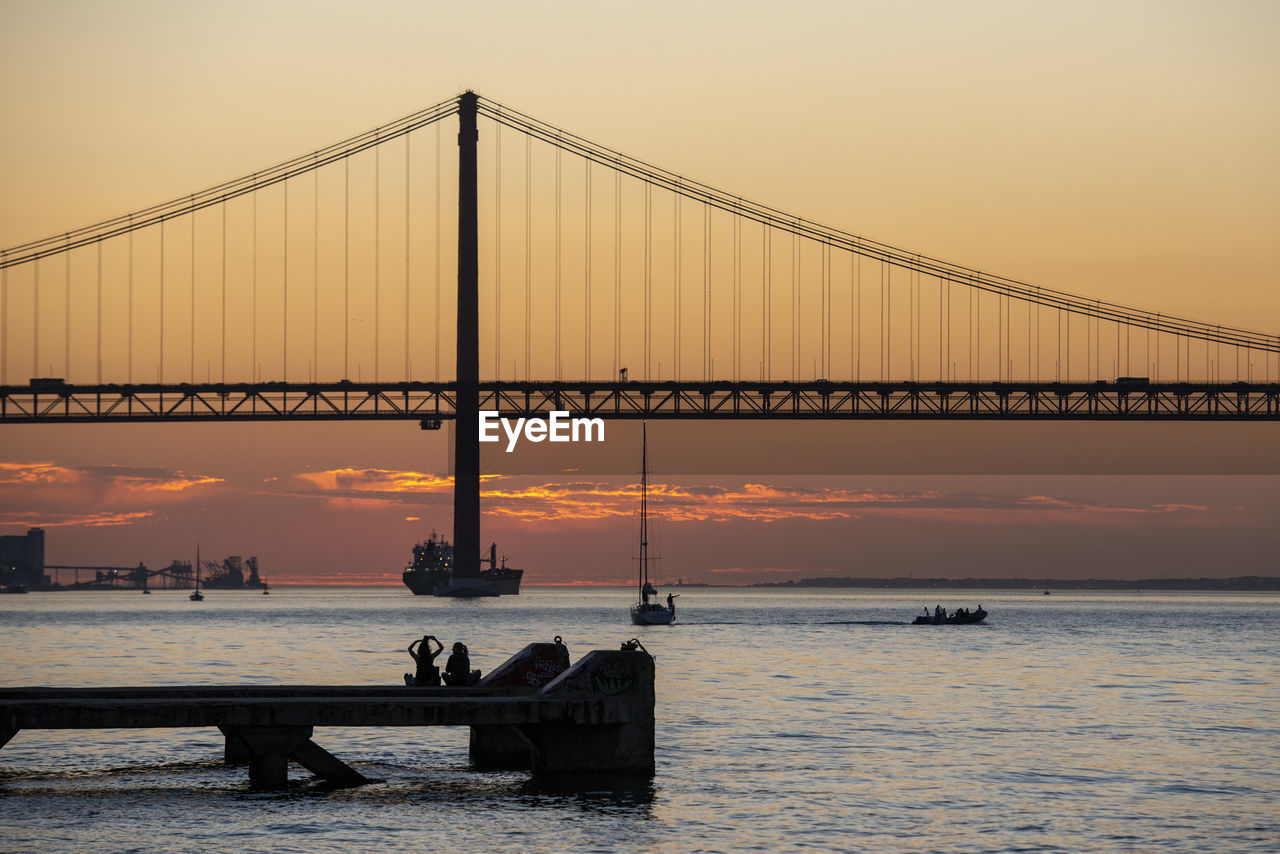 view of suspension bridge over sea at sunset