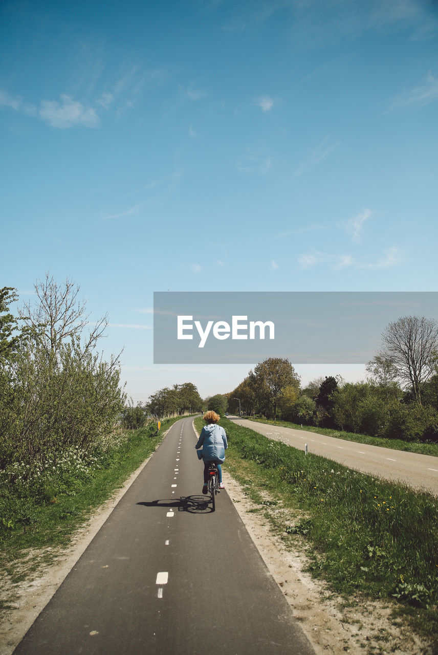 Rear view of woman riding bicycle on road against sky