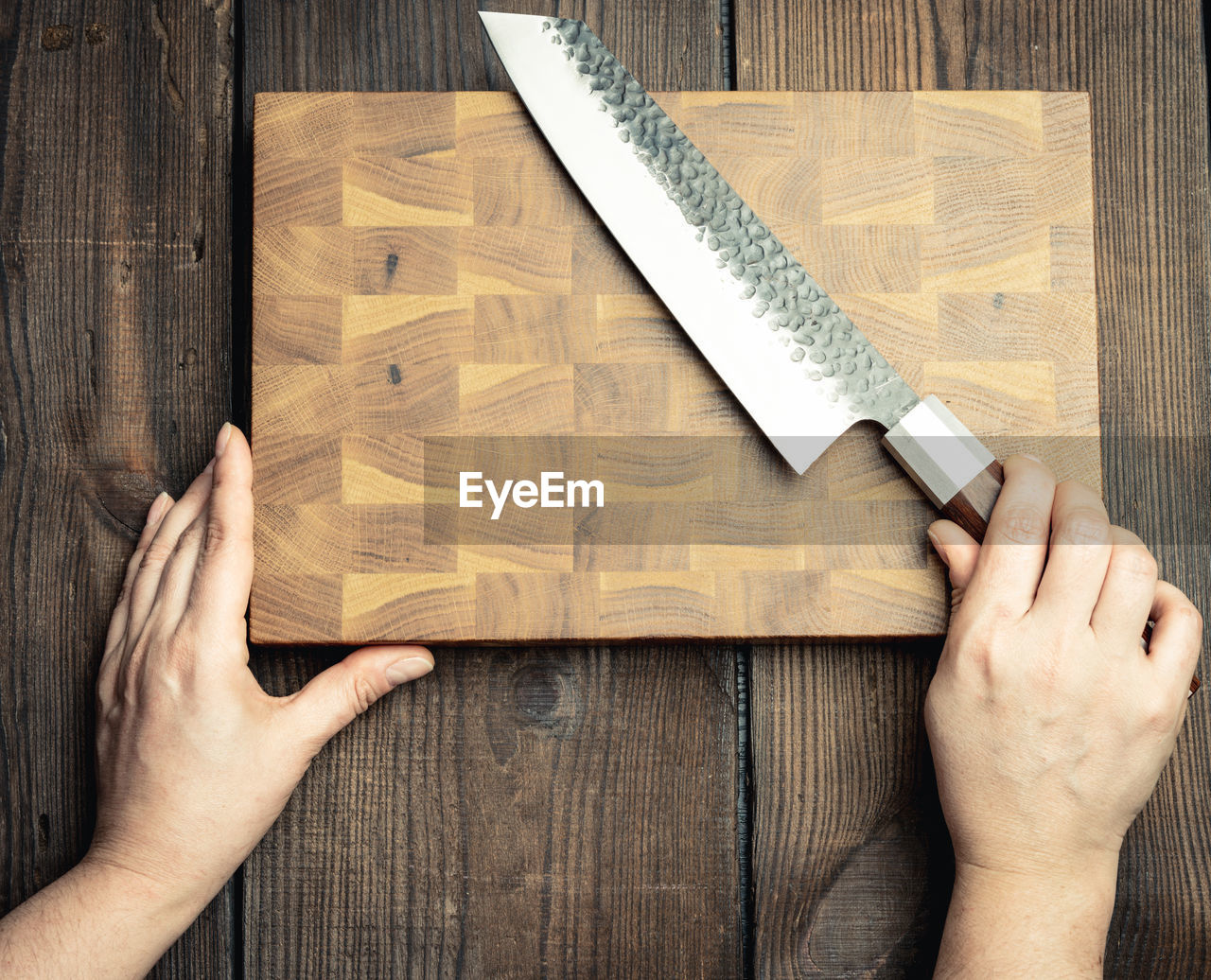 Metal kitchen knife and wooden cutting board on a table made of brown wooden boards, top view