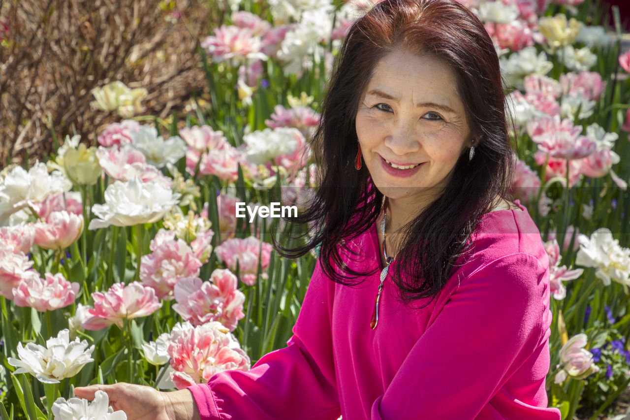 PORTRAIT OF A SMILING WOMAN WITH PINK FLOWER