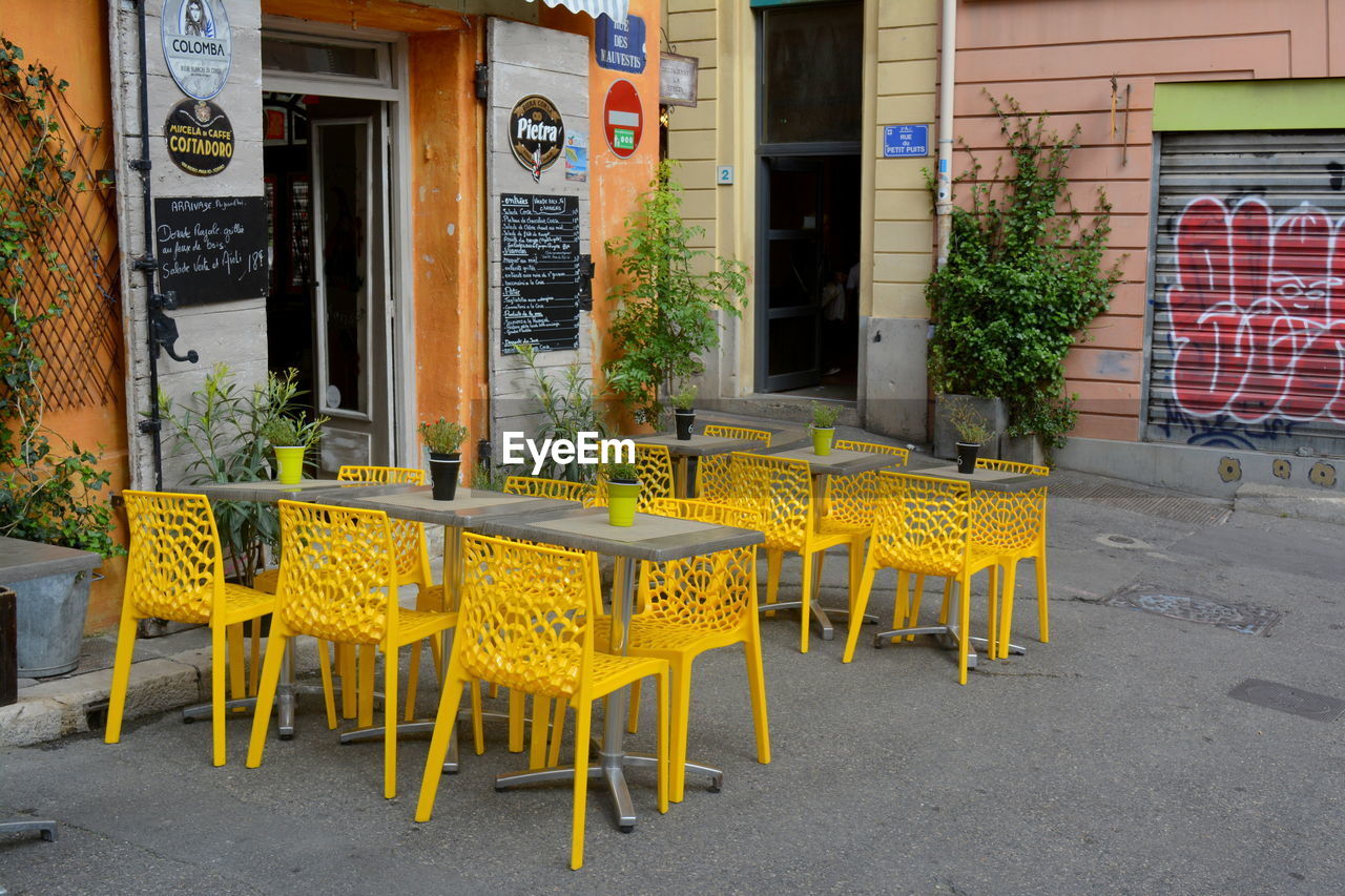 EMPTY CHAIRS AND TABLES AT SIDEWALK CAFE BY BUILDINGS