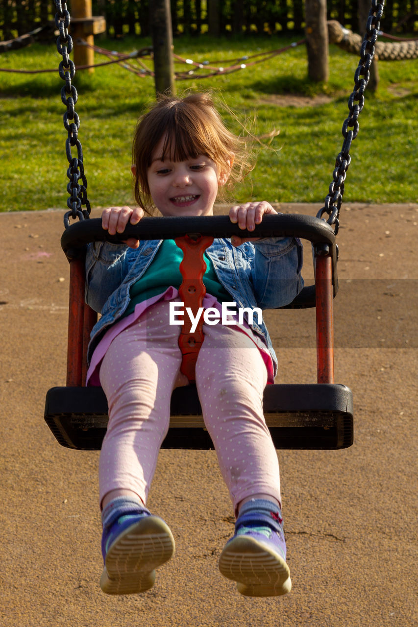 PORTRAIT OF A GIRL SITTING ON SWING AT PLAYGROUND