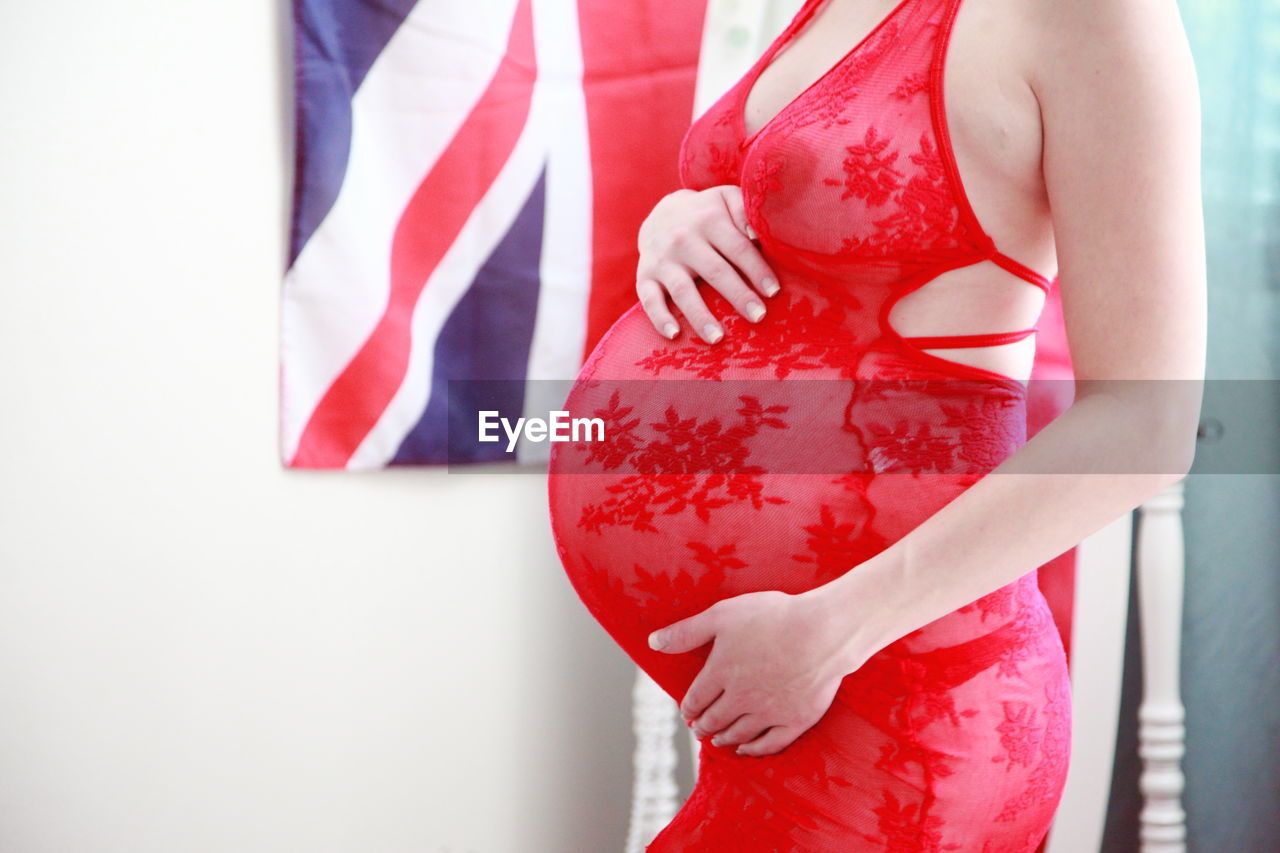 Midsection of pregnant woman with hands on stomach standing at home