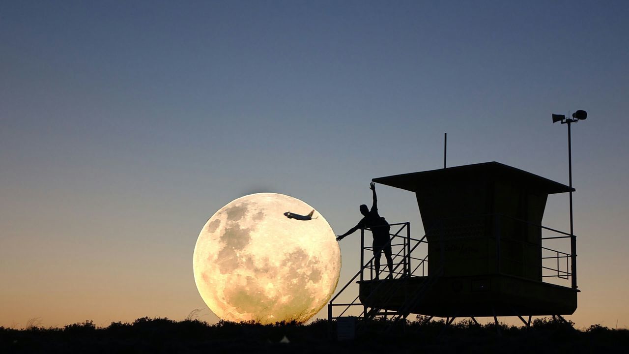 Optical illusion of silhouette man touching full moon against sky