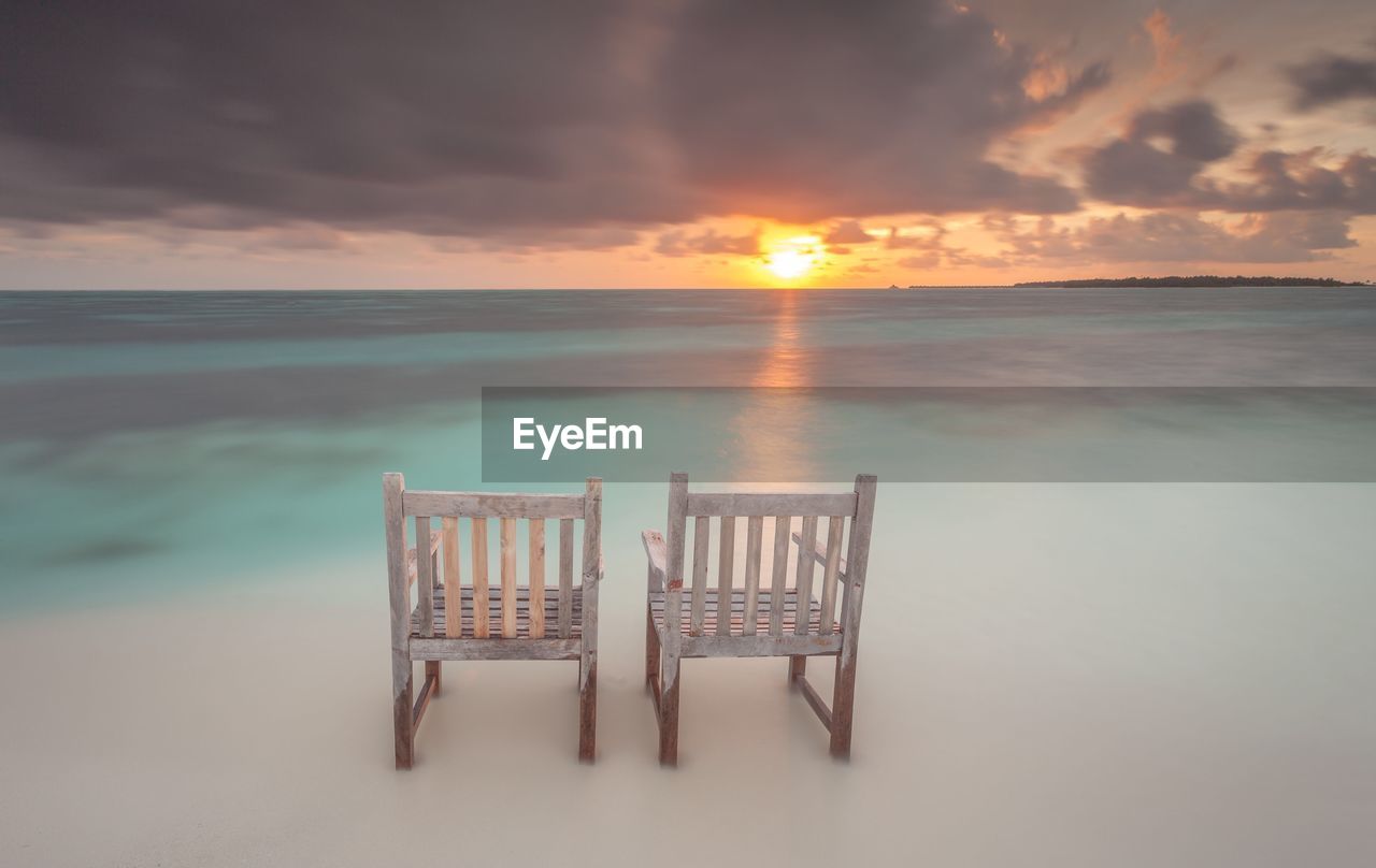 Chairs on beach against cloudy sky during sunset