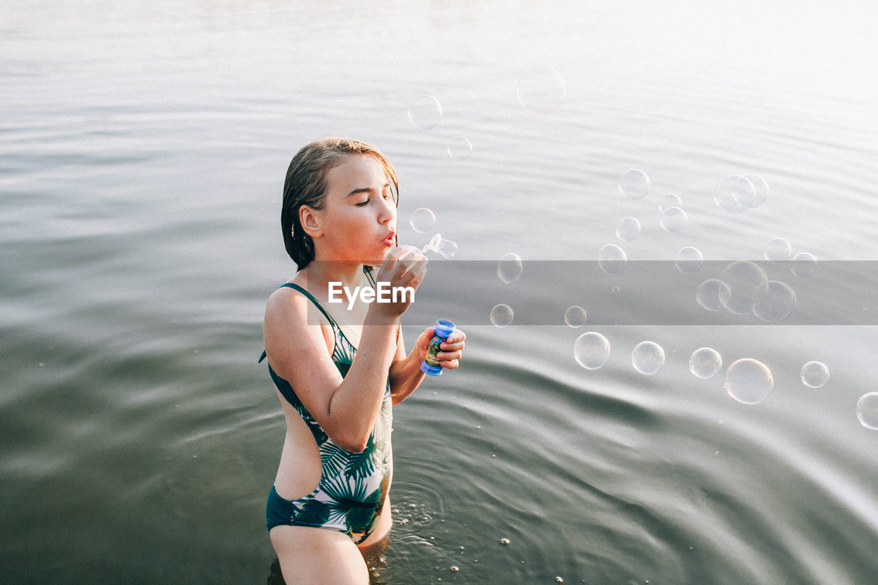 Teenage girl blowing bubbles while standing in lake