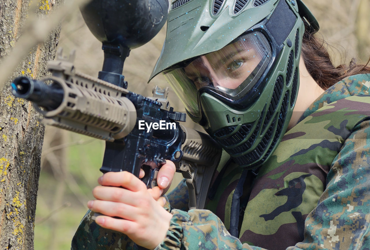 Female army soldier aiming gun while standing in forest