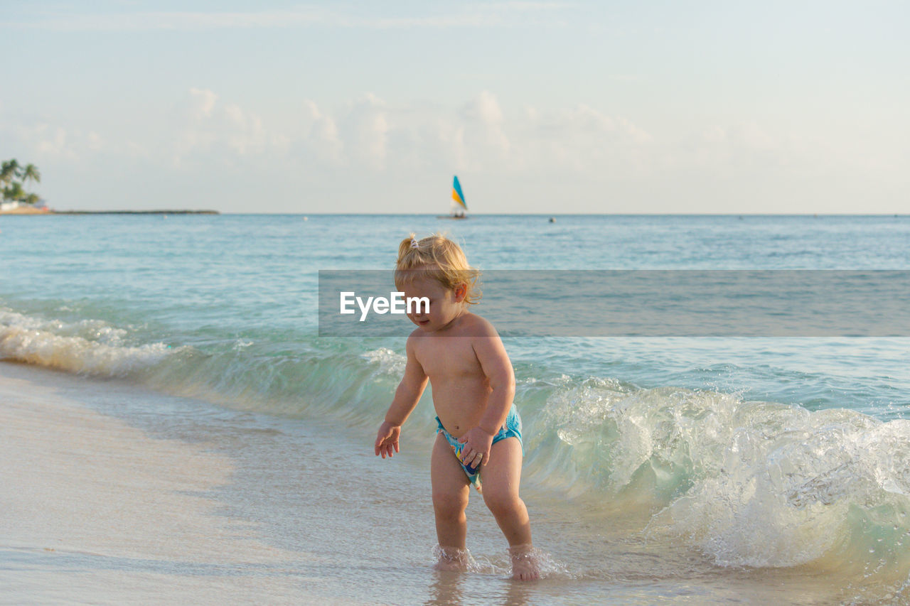 Blond toddler walking in the ocean wave