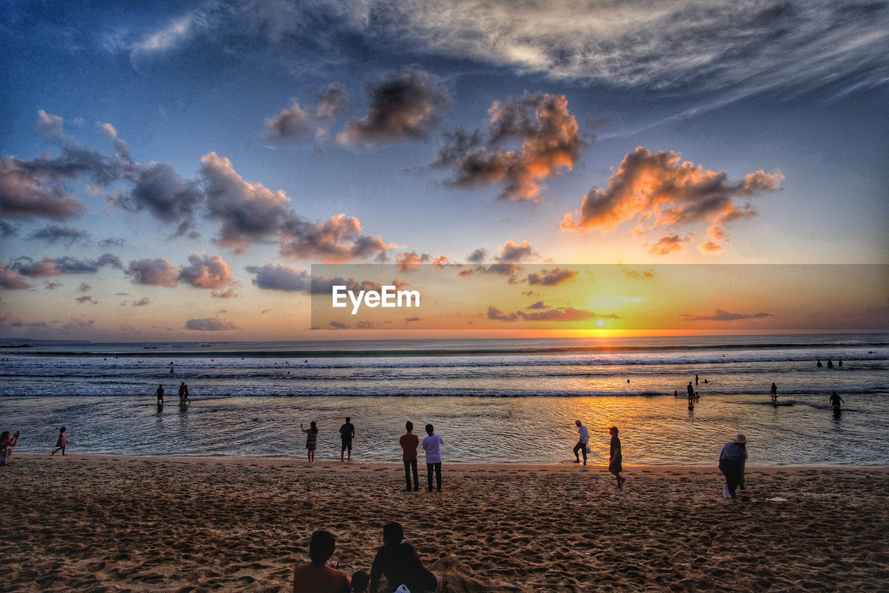 People at beach against sky during sunset