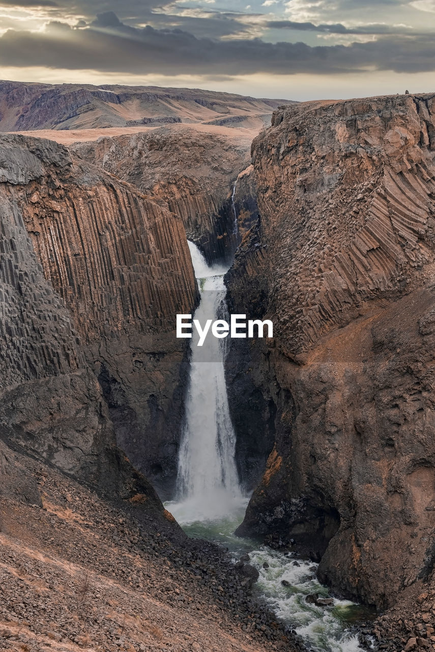 Idyllic litlanesfoss waterfall amidst basalt columns and stream against sky