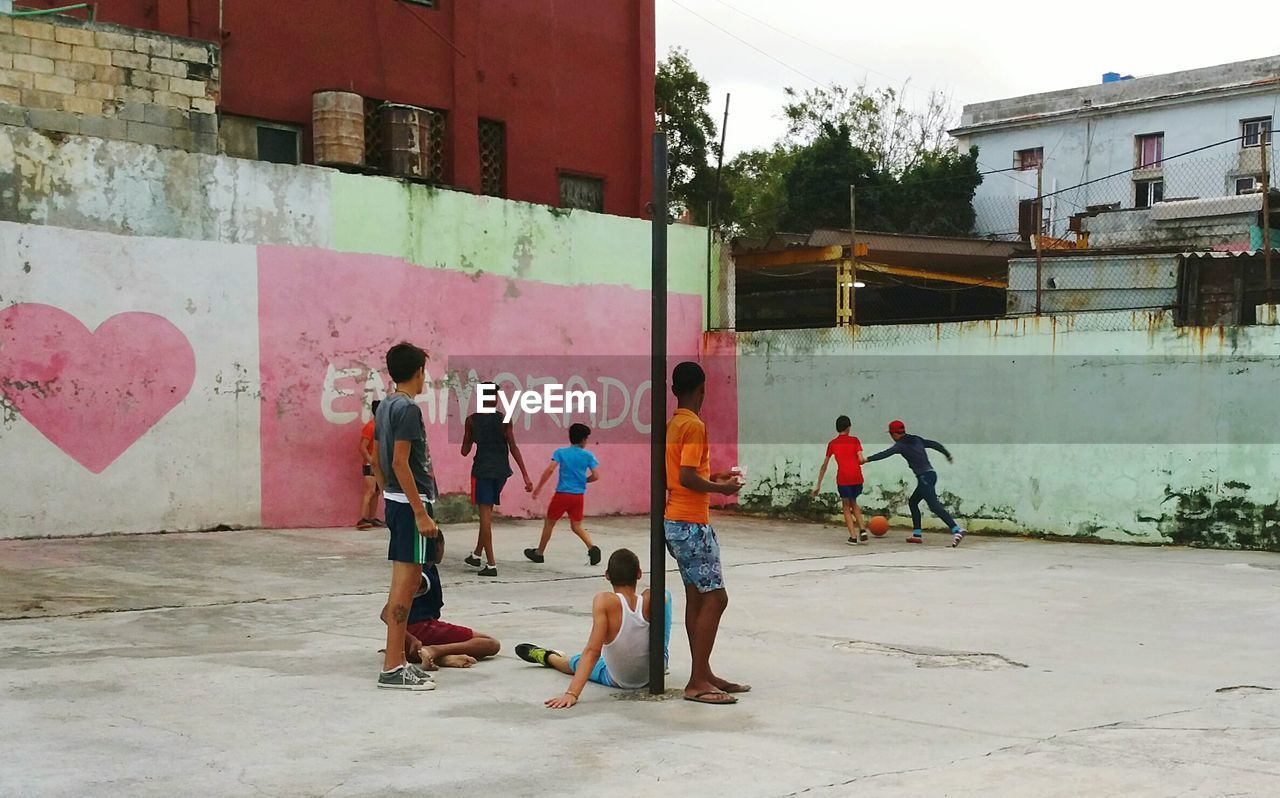 Children playing soccer at playground against buildings
