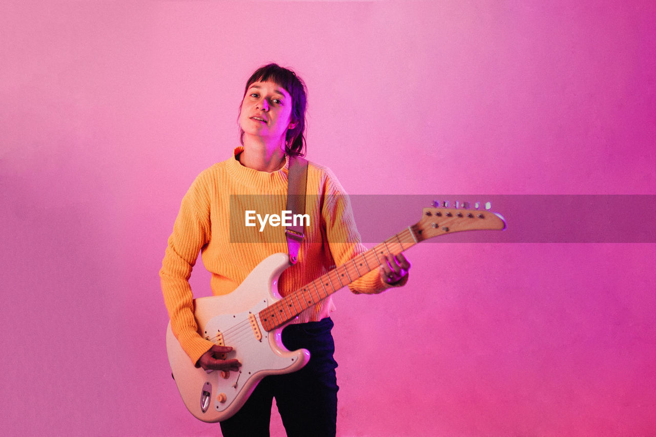 WOMAN PLAYING GUITAR AGAINST PINK WALL