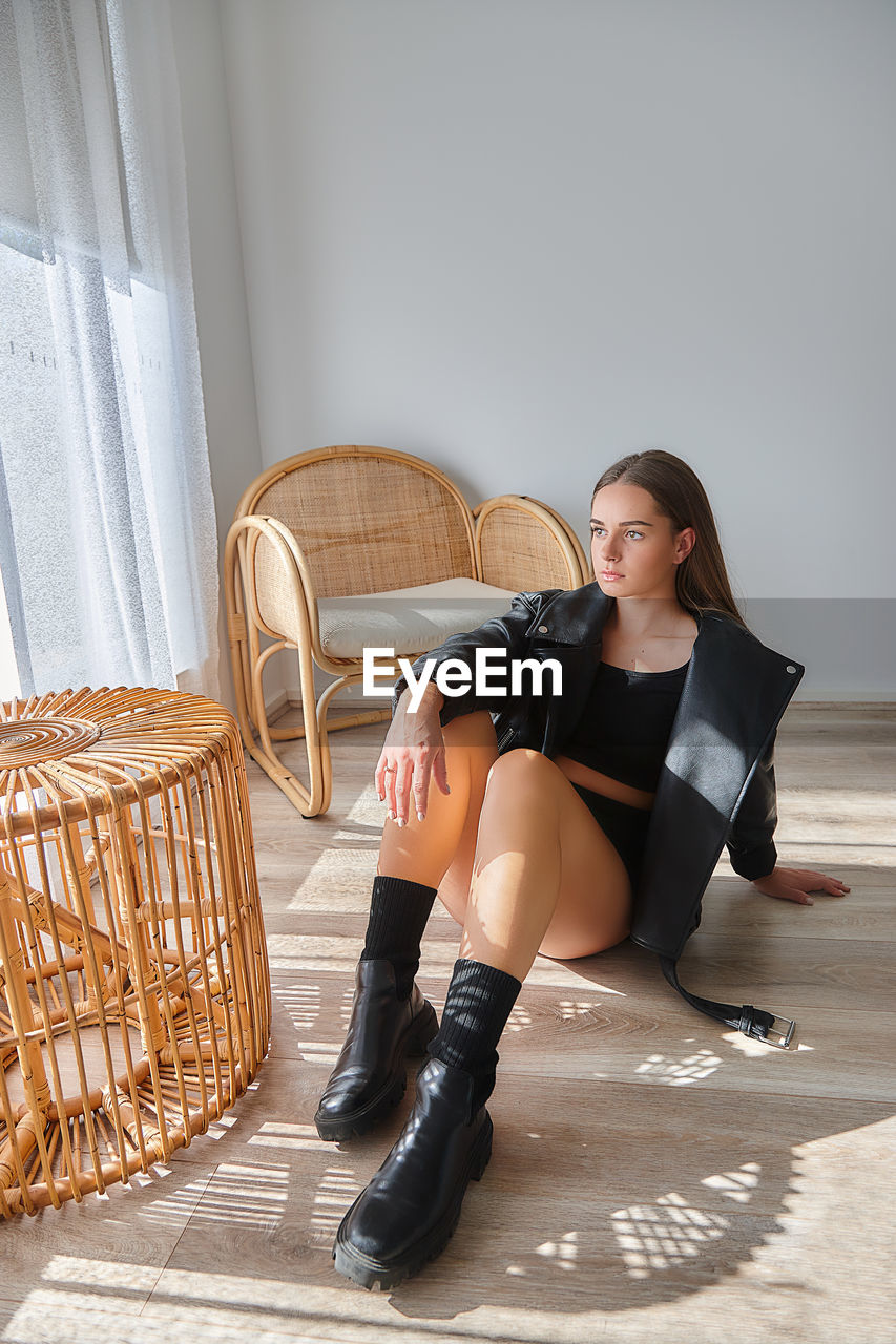 Portrait of young woman sitting on floor at home with black jacket 