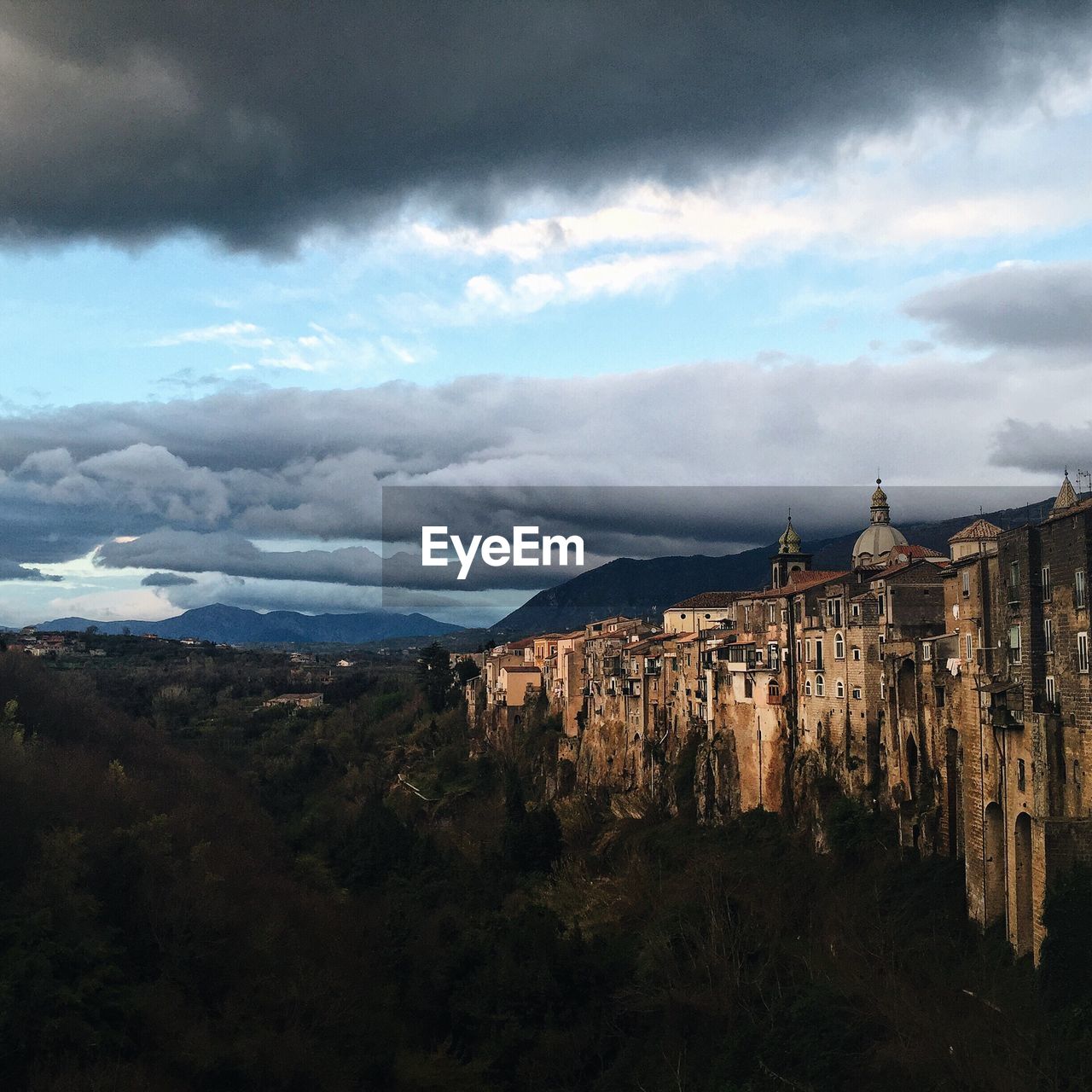 Trees by buildings against cloudy sky at santagata de goti