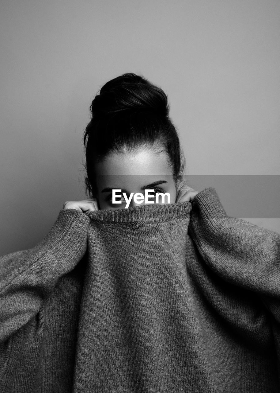 Portrait of young woman covering face with t-shirt against gray background