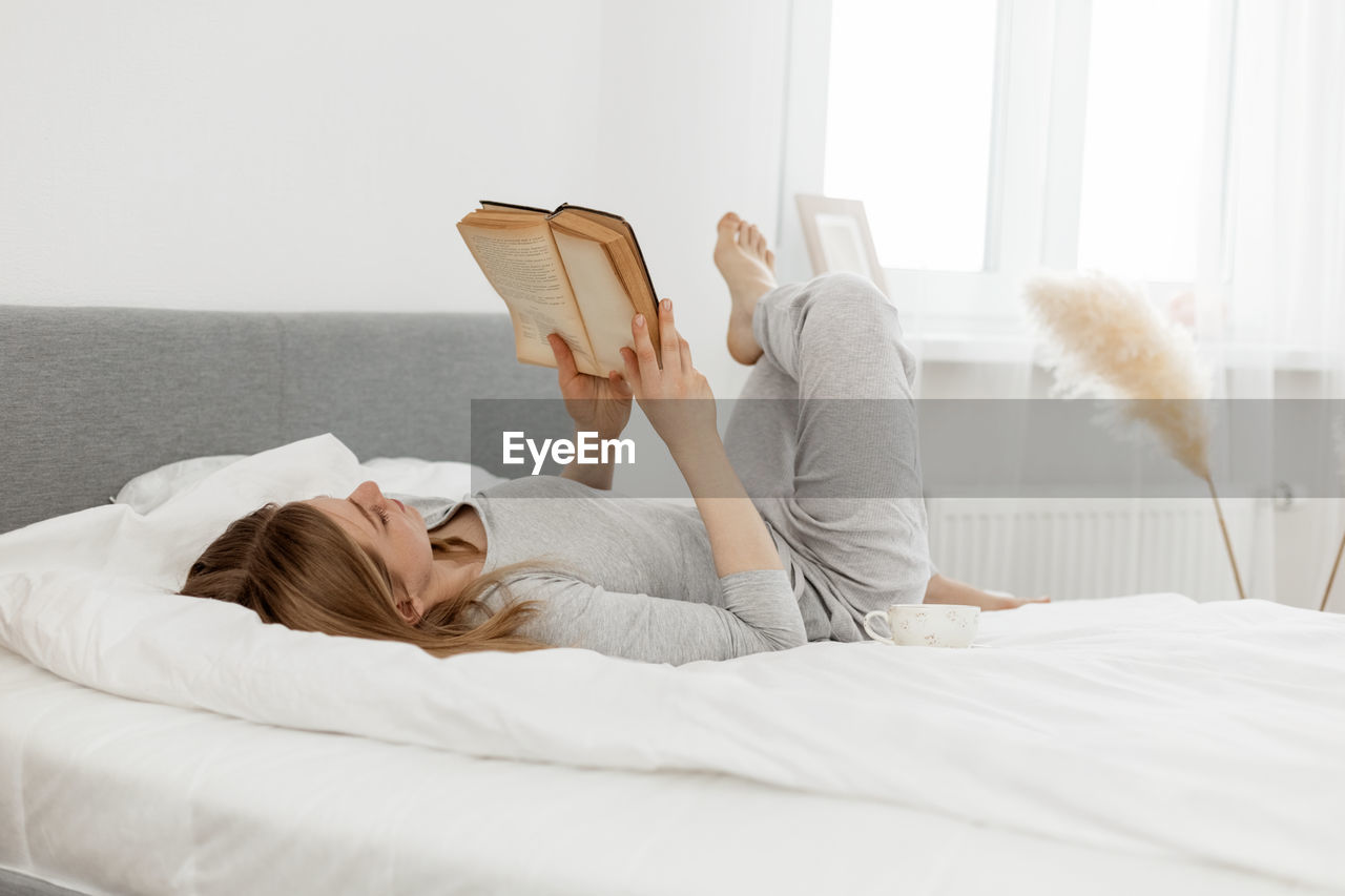 Young girl reading a book while lying on bed at home