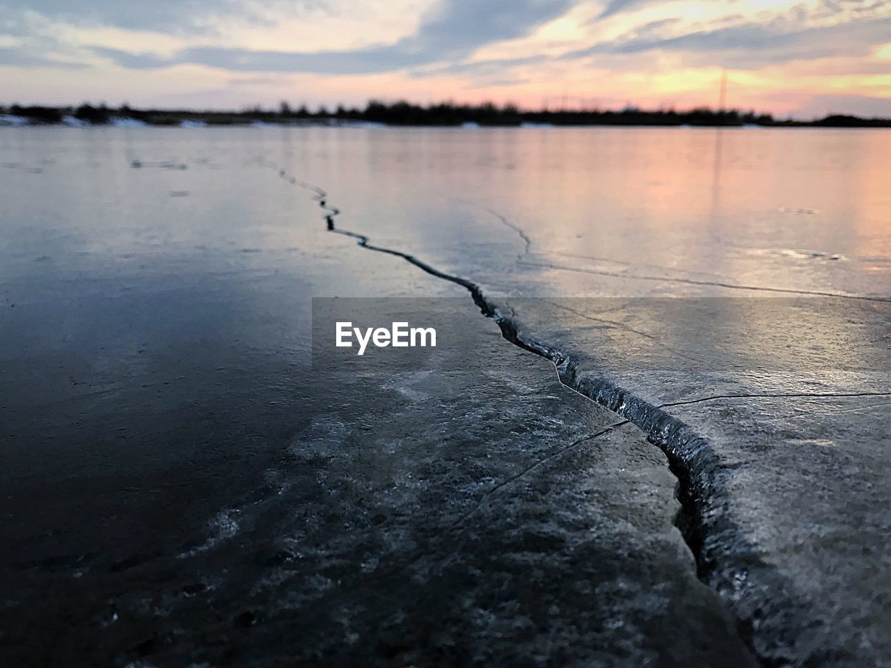 Close-up of frozen lake against sky during sunset