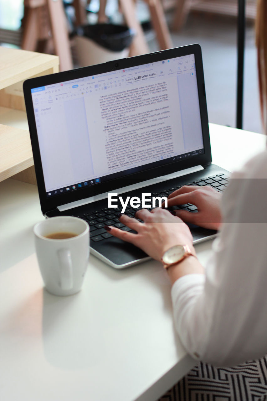 Cropped hand of woman using laptop sitting at table in cafe