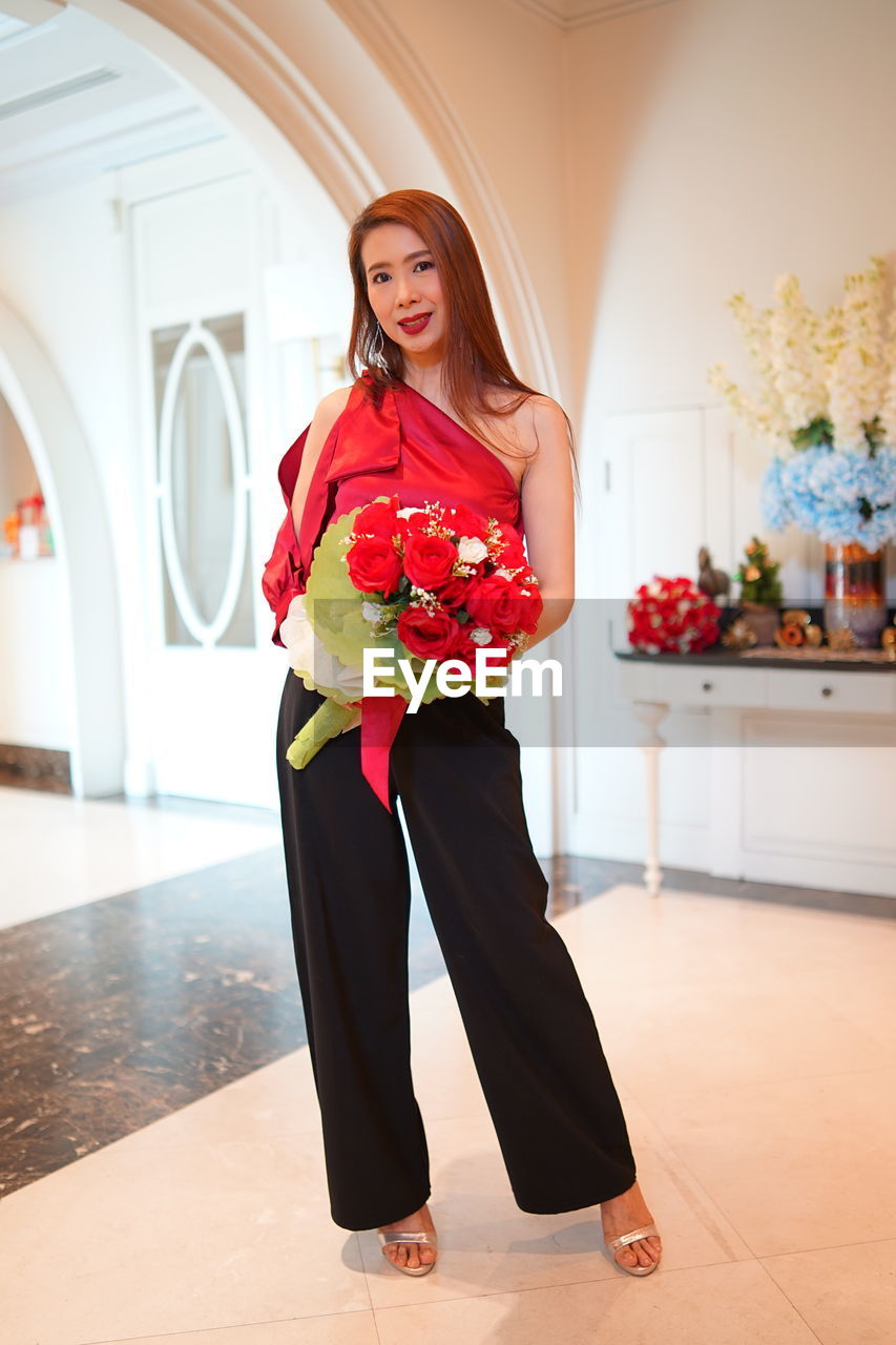 Portrait of woman holding bouquet standing against wall