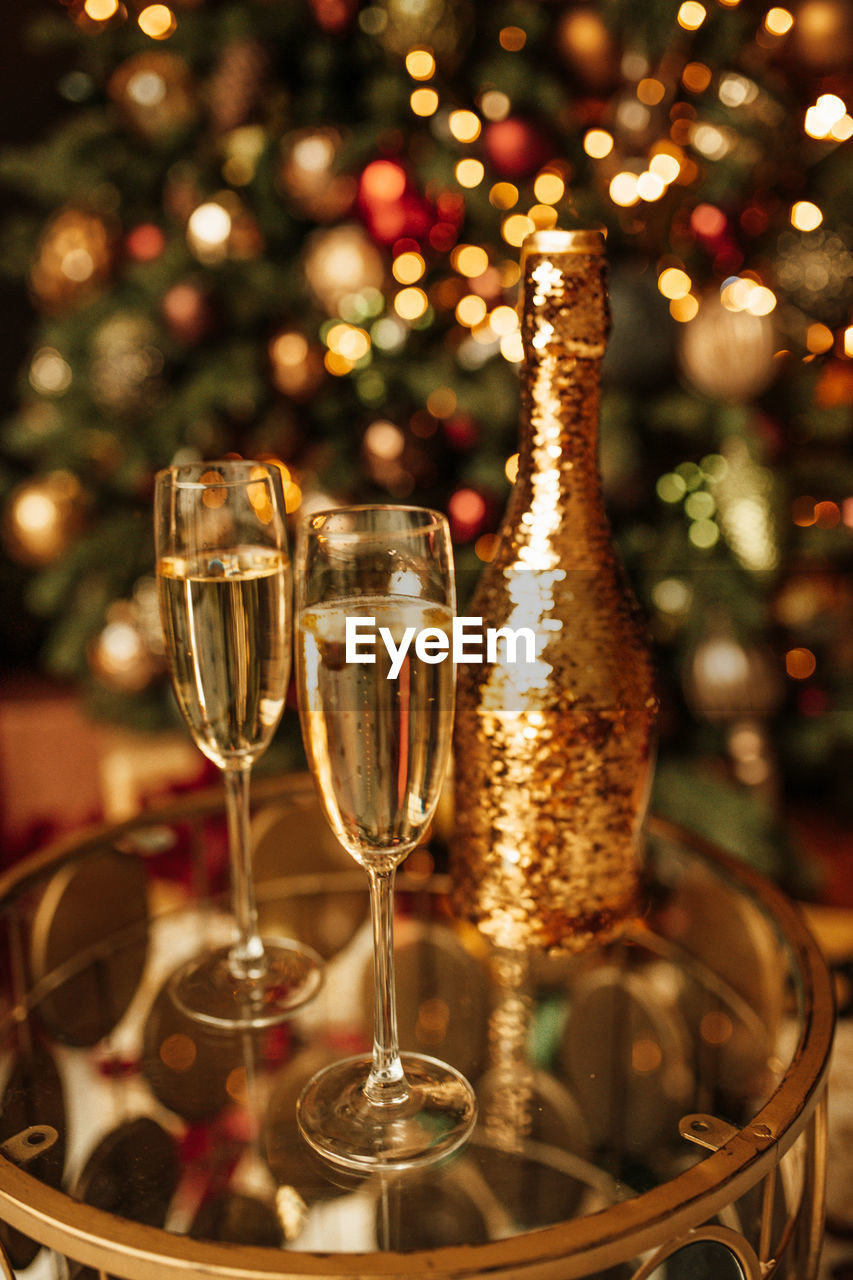 Champagne bottle with golden sequin and glasses at sparkling bokeh yellowish garlands