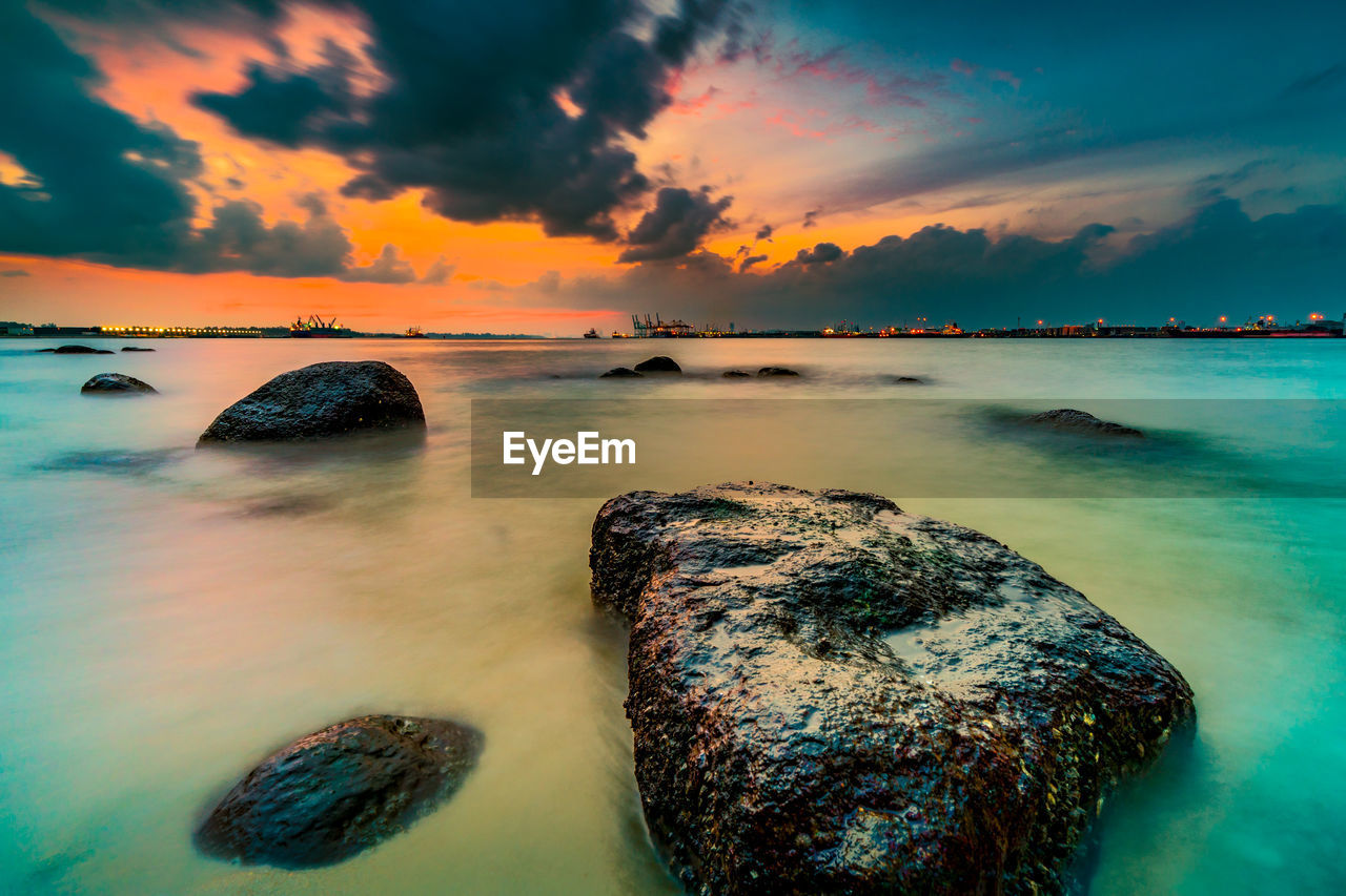 SCENIC VIEW OF ROCKS IN SEA AGAINST SKY DURING SUNSET