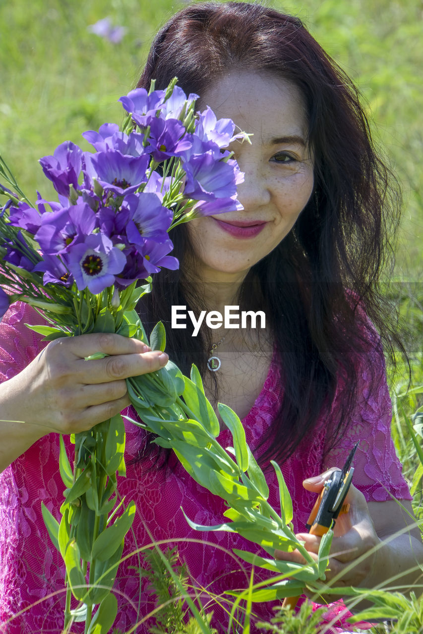 PORTRAIT OF WOMAN HOLDING PURPLE FLOWER