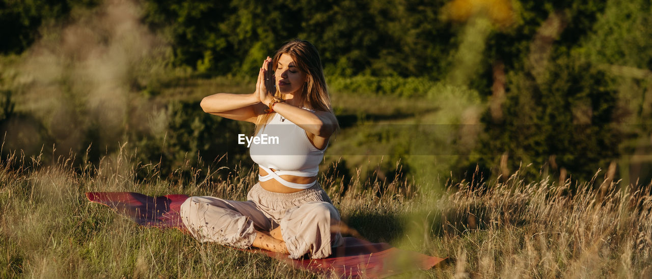 Young woman practicing yoga and meditation on the mat outdoors at sunset with beautiful landscape