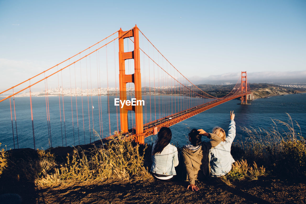 Rear view of women sitting against golden gate bridge