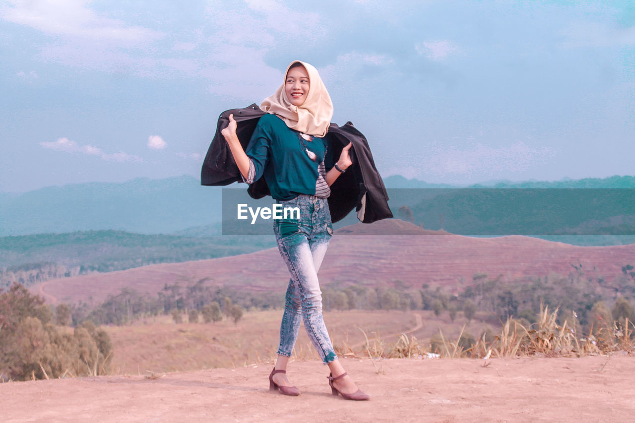 Smiling teenage girl standing on mountain against sky