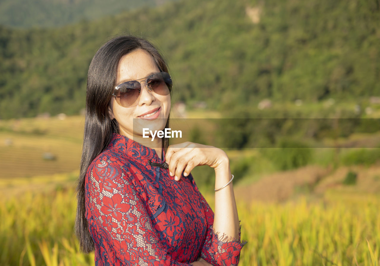 Portrait of smiling young woman wearing sunglasses on field