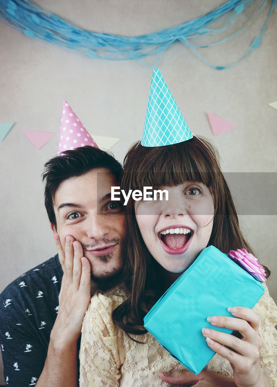 Portrait of smiling friends wearing party hat against wall at home