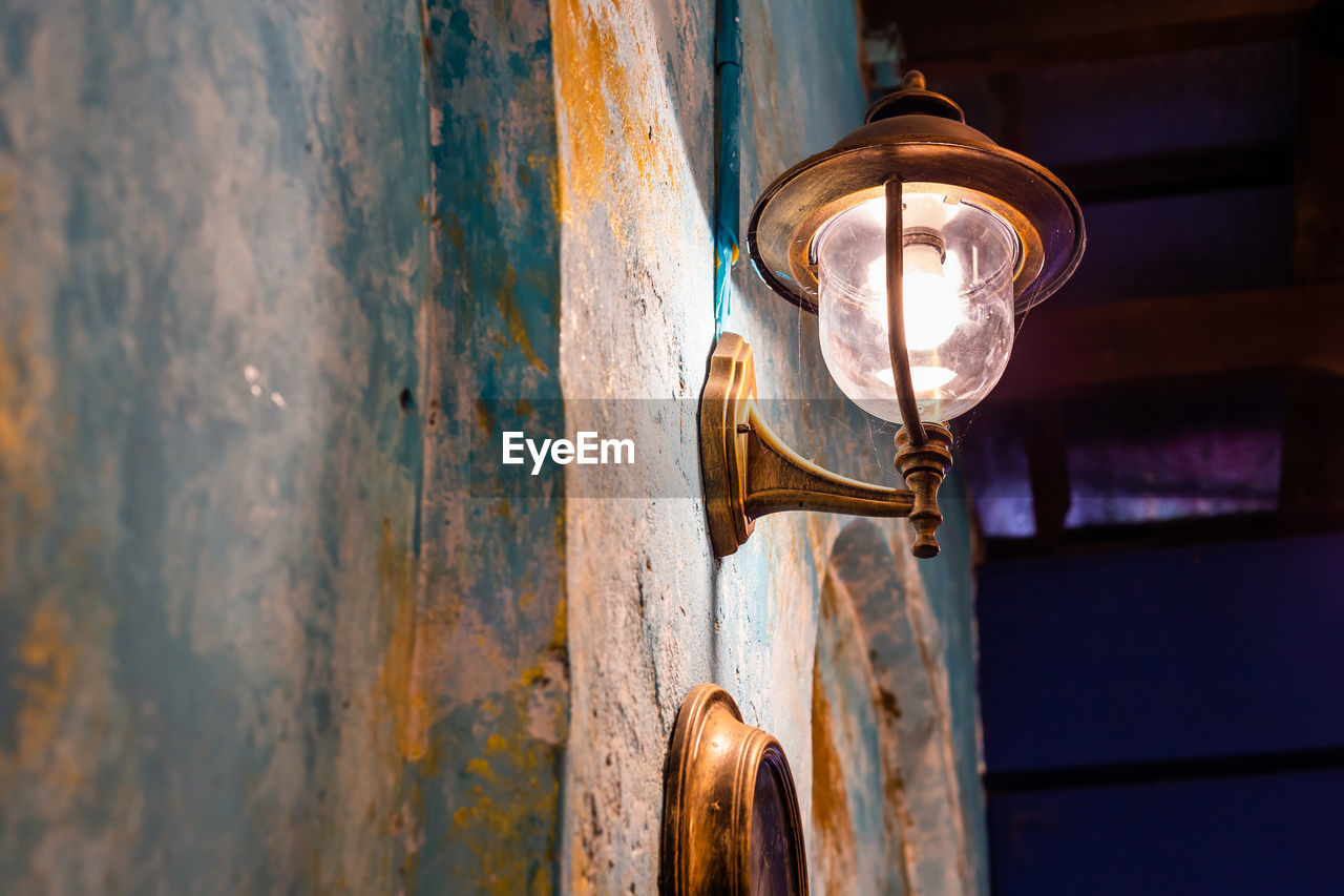 LOW ANGLE VIEW OF ILLUMINATED LIGHT BULB AGAINST WALL