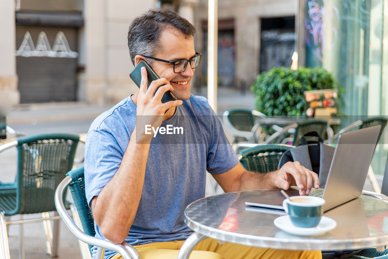 Smiling man talking on phone while sitting at cafe