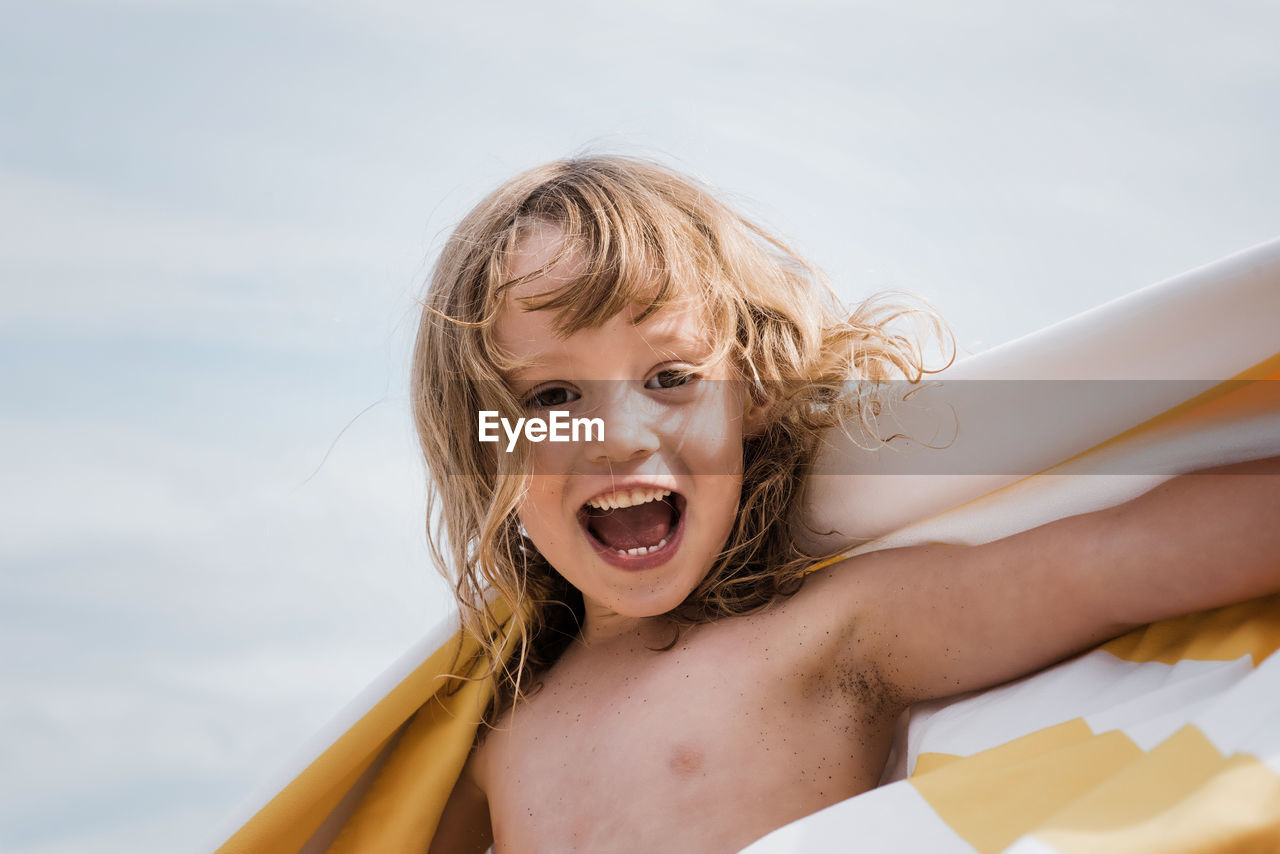 Girl laughing whilst wrapped in a striped towel at the beach