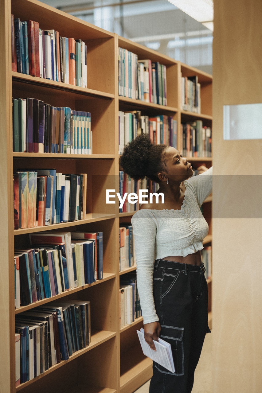 Female student searching books on shelf in library at university