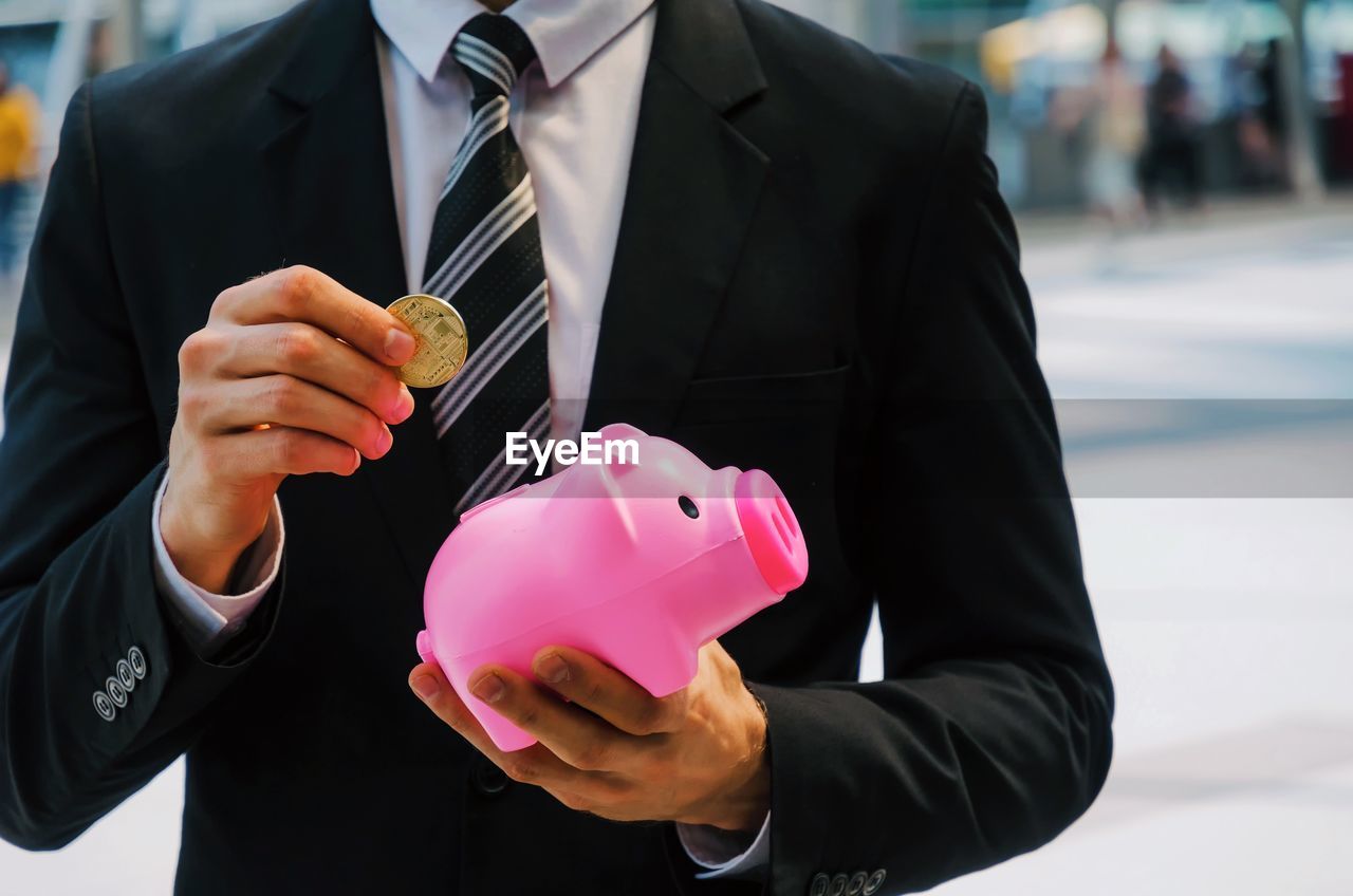 Midsection of businessman inserting coin in pink piggy bank