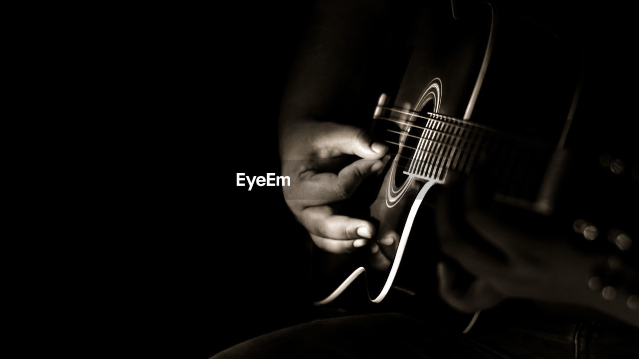 Cropped image of man playing guitar against black background