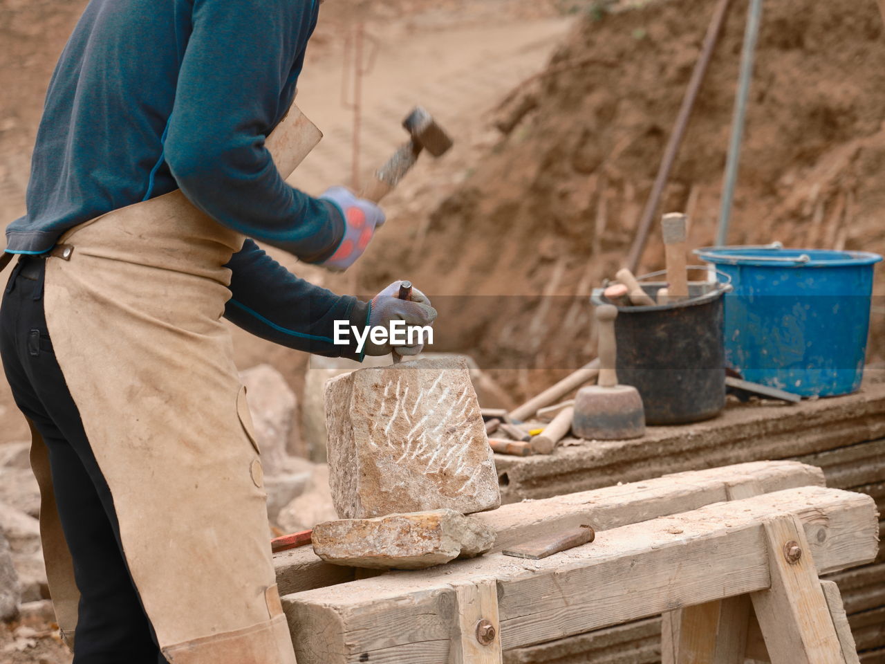 Midsection of craftsperson using hammer and chisel on rock