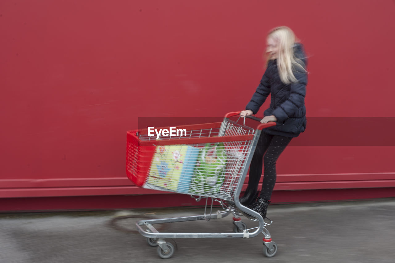 Playful girl on shopping cart against wall