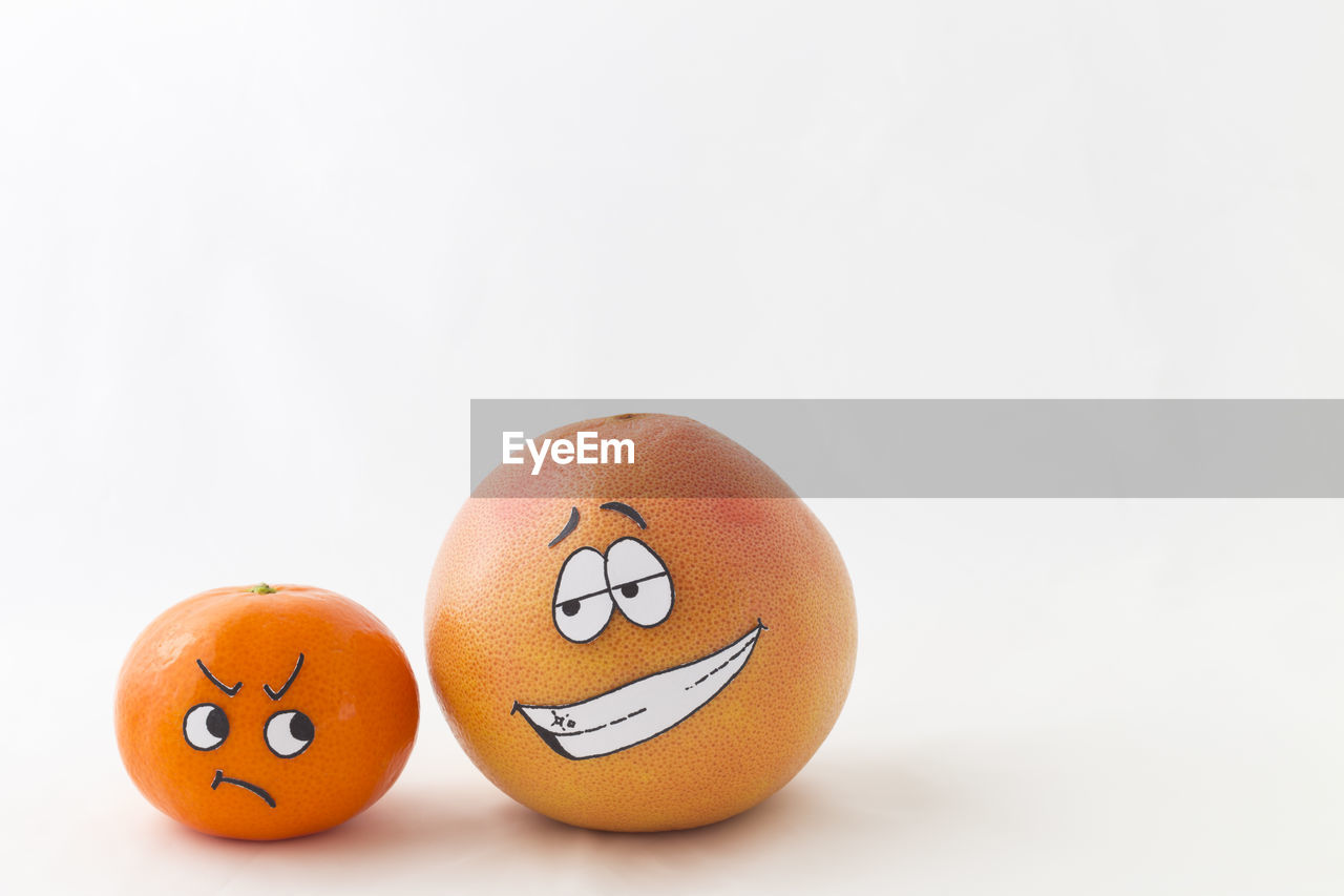 Close-up of anthropomorphic face on fruits over white background